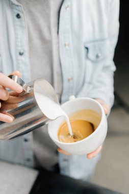 Barista özel kahve dükkanında latte yapıyor. Profesyonel bir adam espresso ile süt dolduruyor.