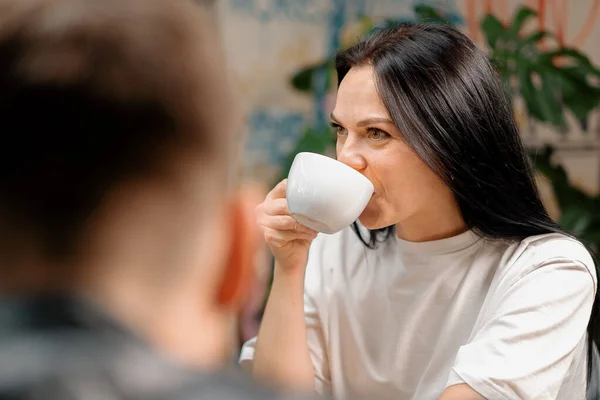 Girl drinks filter coffee in the company of cheerful friends who communicate on weekends and spend time together at lunch in the cafeteria. Meeting in a public place. Friendship.