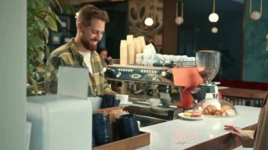 Handsome male barista gives coffee to a girl. Girl buys coffee in a coffee shop.