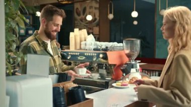 Handsome male barista gives coffee to a girl. Girl buys coffee in a coffee shop.