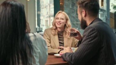 Beautiful hipster girl is having fun in the company of happy friends in a coffee shop. Friends drink coffee.