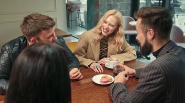 Beautiful hipster girl is having fun in the company of happy friends in a coffee shop. Friends drink coffee.