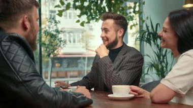 Handsome stylish hipster guy laughs in a coffee shop in the company of cheerful friends.