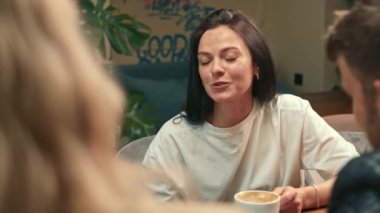 A white-skinned girl drinks filter coffee in a coffee shop in the company of cheerful friends.