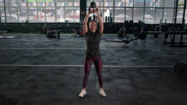 Young female athlete trains with a kettlebell in the gym, squats with a kettlebell