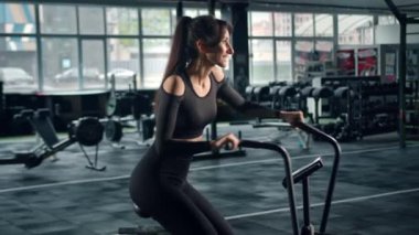 Young female athlete trains cardio on a bicycle with a fan, cardio training