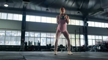 Young female athlete trains with a kettlebell in the gym, squats with a kettlebell