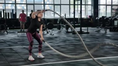 Young female athlete trains in the gym with ropes, crossfit, endurance