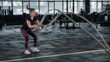Young female athlete trains in the gym with ropes, crossfit, endurance