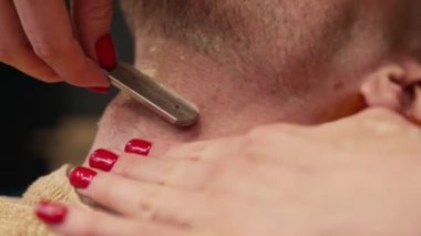 Barbershop: woman barber shaves a man using a straight razor