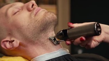 Barbershop: woman hairdresser cuts a man's beard with razor