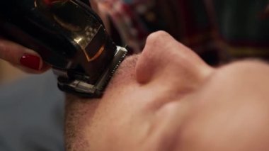 Barbershop: woman hairdresser cuts a man's beard with razor
