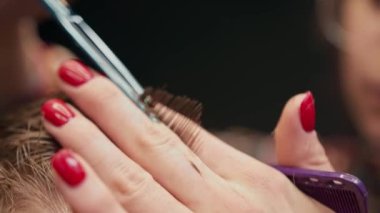 Barbershop, close-up: woman barber cuts a men's hair with scissors