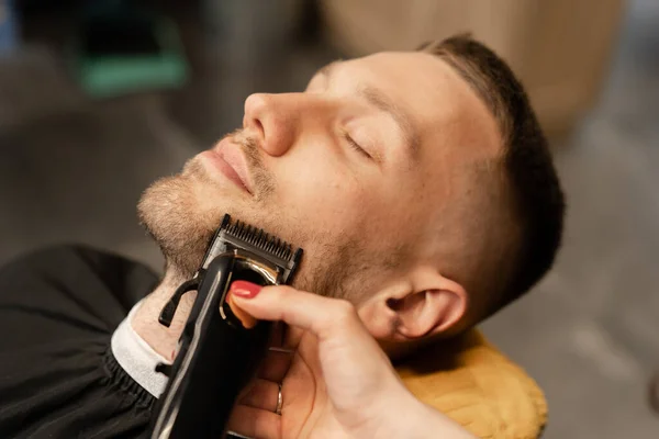 Barbershop, close-up: a woman barber shaves mans beard with a razor