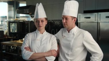 Professional kitchen, portrait: Female and Male Chef stand side by side in the background of kitchen, smiling