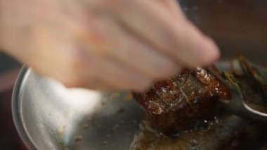 Close-up: Chef pouring sauce over a filet mignon while cooking