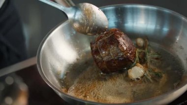 Close-up: Chef pouring sauce over a filet mignon while cooking