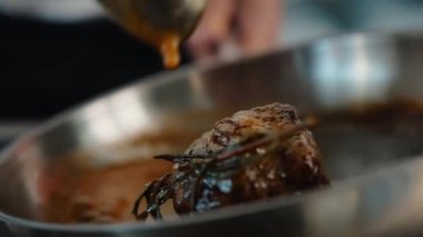 Close-up: Chef pouring sauce over a filet mignon while cooking