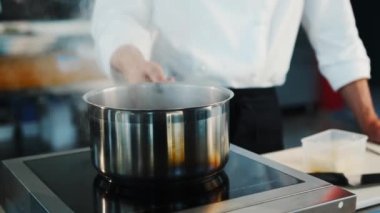 The chef makes sauce in a saucepan in a professional restaurant kitchen. The process of food preparation.
