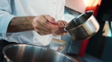 The chef makes sauce in a saucepan in a professional restaurant kitchen. The process of food preparation.