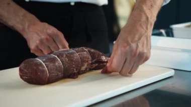 Close-up of the chef tying the meat with a filet mignon string. The process of preparing food in restaurant.