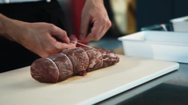 Close-up of the chef tying the meat with a filet mignon string. The process of preparing food in restaurant.
