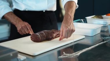 Close-up of the chef tying the meat with a filet mignon string. The process of preparing food in restaurant.