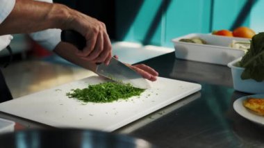 Professional kitchen of the restaurant, close-up: The chef cuts the greens herbs finely with knife