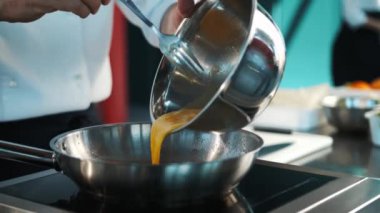 Professional restaurant kitchen, close-up: Chef pouring eggs into frying pan, preparing an omelet