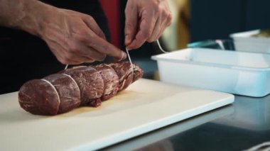 Close-up of the chef tying the meat with a filet mignon string. The process of preparing food in restaurant.