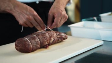 Close-up of the chef tying the meat with a filet mignon string. The process of preparing food in restaurant.