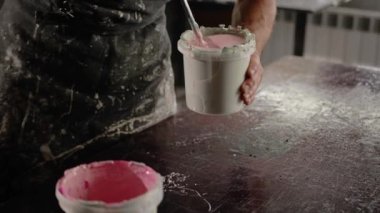 A male handyman mixes paint in a can in a workshop. Sculptor mixes resin with paint to create a vase.