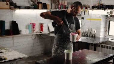 A male handyman mixes paint in a can in a workshop. Sculptor mixes resin with paint to create a vase.