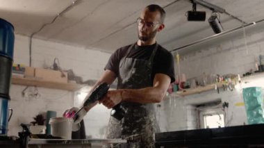 A male handyman mixes paint in a can in a workshop. Sculptor mixes resin with paint to create a vase.