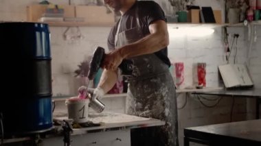 A male handyman mixes paint in a can in a workshop. Sculptor mixes resin with paint to create a vase.