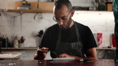 A man of Arab appearance sharpens a blade in workshop. Sculptor, painter, needleworker.