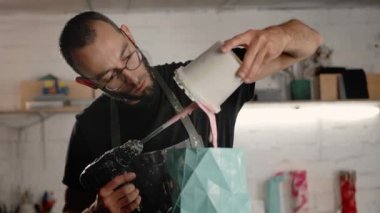 Male sculptor handyman creates handmade vase. The paint is poured into the object.