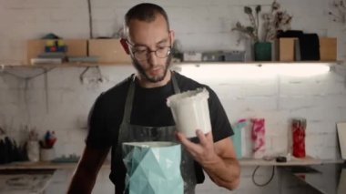 Male sculptor handyman creates handmade vase. The paint is poured into the object.