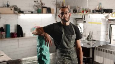 Portrait of a man: male artisan sculptor looks at the camera against the backdrop of a workshop, tools and products