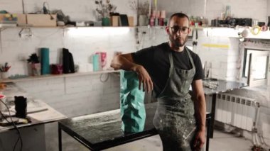 Portrait of a man: male artisan sculptor looks at the camera against the backdrop of a workshop, tools and products