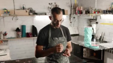 Male portrait: man smokes a cigarette in a workshop.. The sculptor is tired and resting.