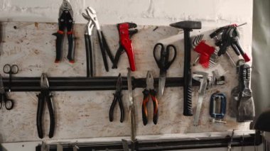 Workshop: male artisan artist sculptor takes tool from the wall. Pliers, hammer, scissors, spatula, blades