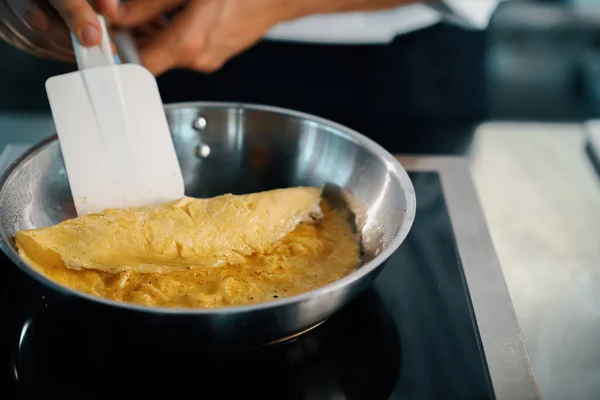 Close-up of a chef preparing a french omelette on a frying pan in professional kitchen