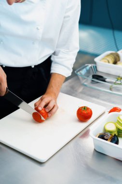 Close-up of chef slicing tomato in a professional restaurant kitchen