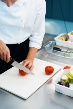 Close-up of chef slicing tomato in a professional restaurant kitchen