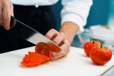Close-up of chef slicing tomato in a professional restaurant kitchen