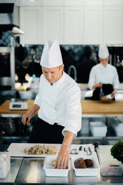 Professional kitchen: two chefs prepare food. The cook cuts mushrooms to prepare delicious dish.