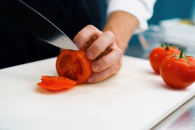 Close-up of chef slicing tomato in a professional restaurant kitchen