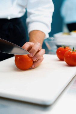 Close-up of chef slicing tomato in a professional restaurant kitchen
