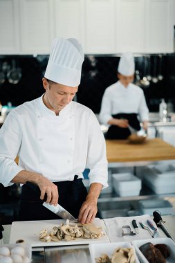 Professional kitchen: two chefs prepare food. The cook cuts mushrooms to prepare delicious dish.